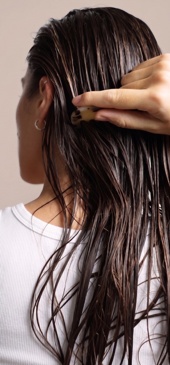 immagine di una ragazza vista di spalle con capelli bagnati e una mano che si tocca i capelli