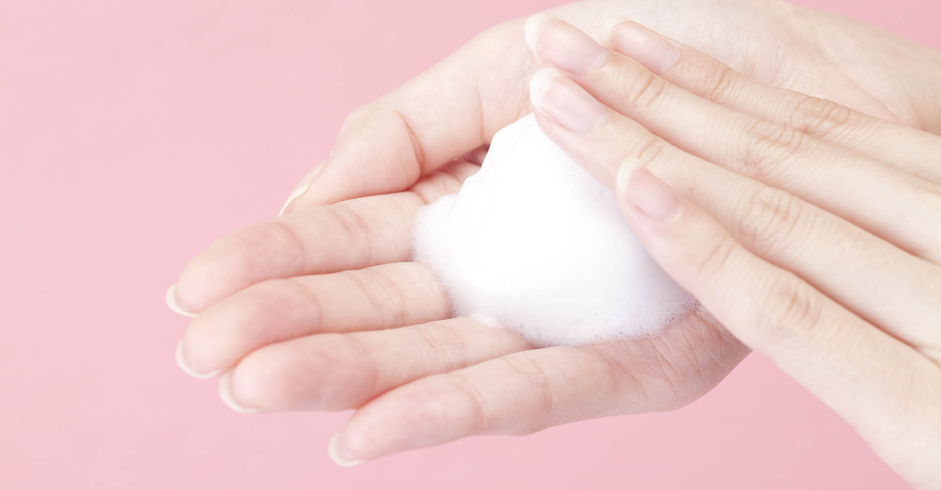 una mano con all'interno un pugno di mousse bianca. Sfondo neutro rosa