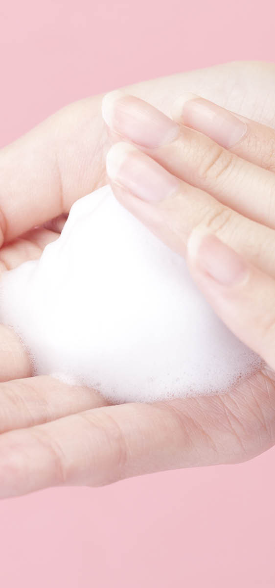 una mano con all'interno un pugno di mousse bianca. Sfondo neutro rosa