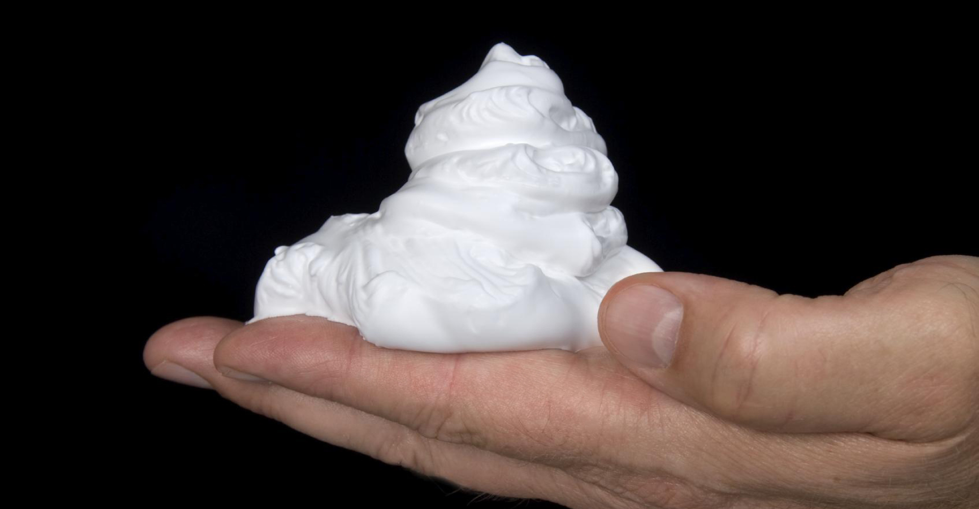 immagine di una mano di un uomo su sfondo nero, con sopra una noce di mousse bianca.